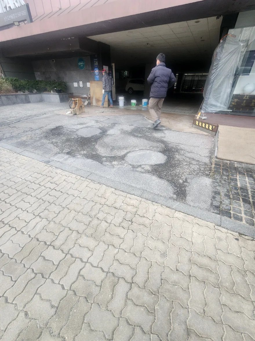 건물 진입 통로 바닥의 기존 포장이 닳고 깨진 상태를 확인하는 단계로 보입니다.