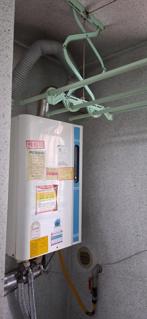 벽면에 가스보일러가 새로 설치되어 있고, 제품 라벨과 안내 스티커가 그대로 부착된 상태입니다.
