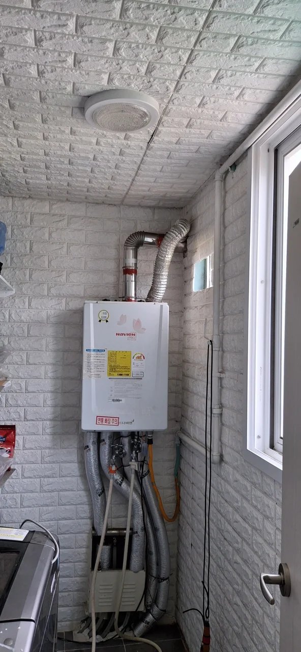 앞서 사진과 같은 벽돌무늬 벽면에 Navien 보일러가 설치되어 있고, 천장 환풍기 바로 아래 위치해 있습니다.