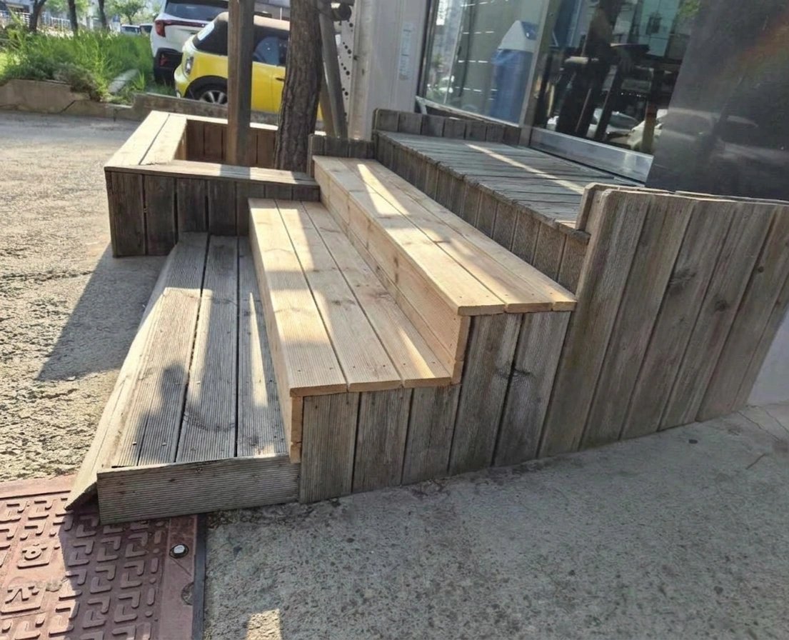 앞 사진과 같은 상가 앞 데크 단을 손본 상태로, 일부 각재가 새 목재로 교체되어 밝은 색으로 드러나 있습니다.
