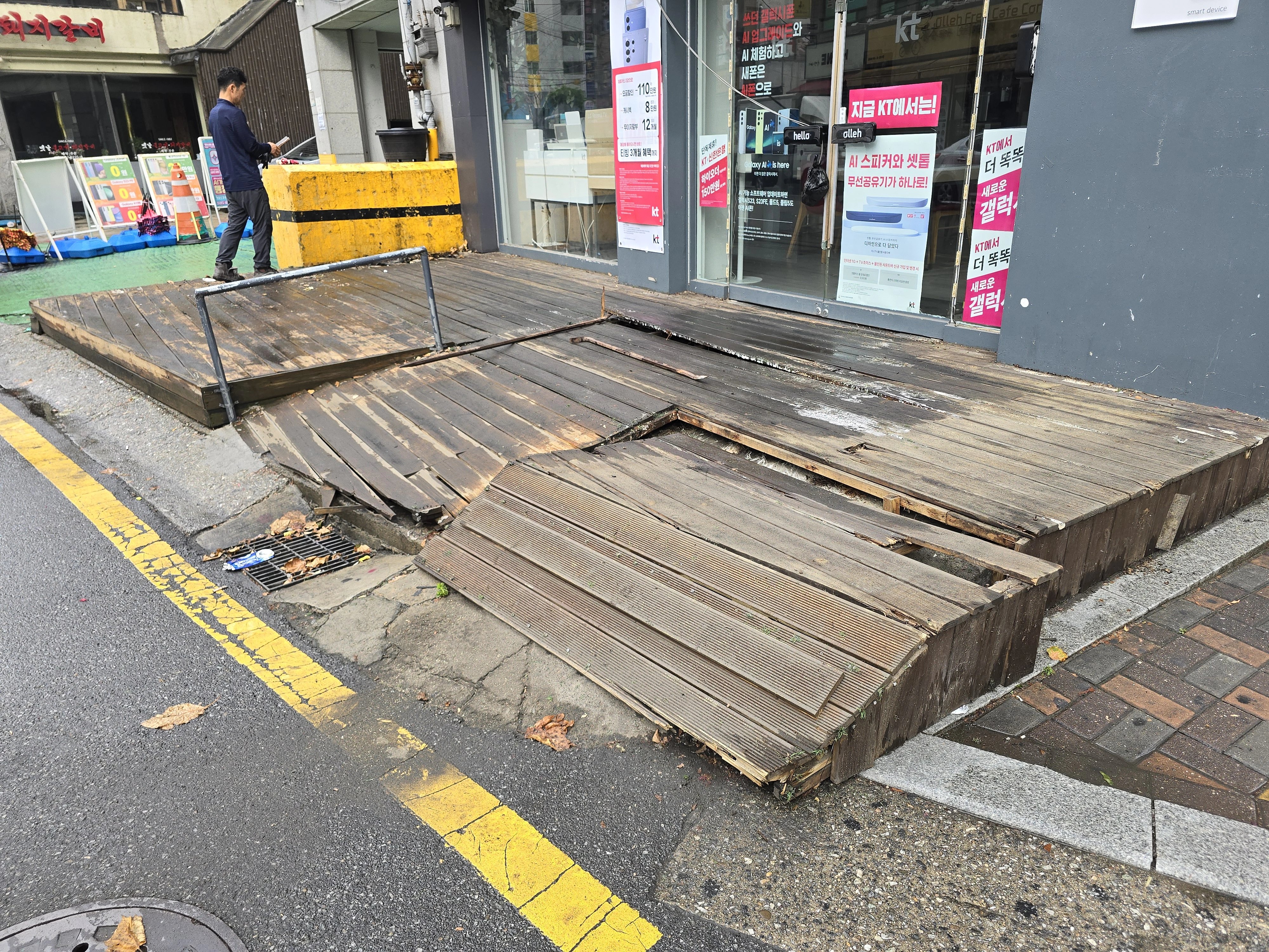 오래된 목재 데크가 해체되어 인도 한쪽에 겹쳐 쌓여 있는 모습입니다.