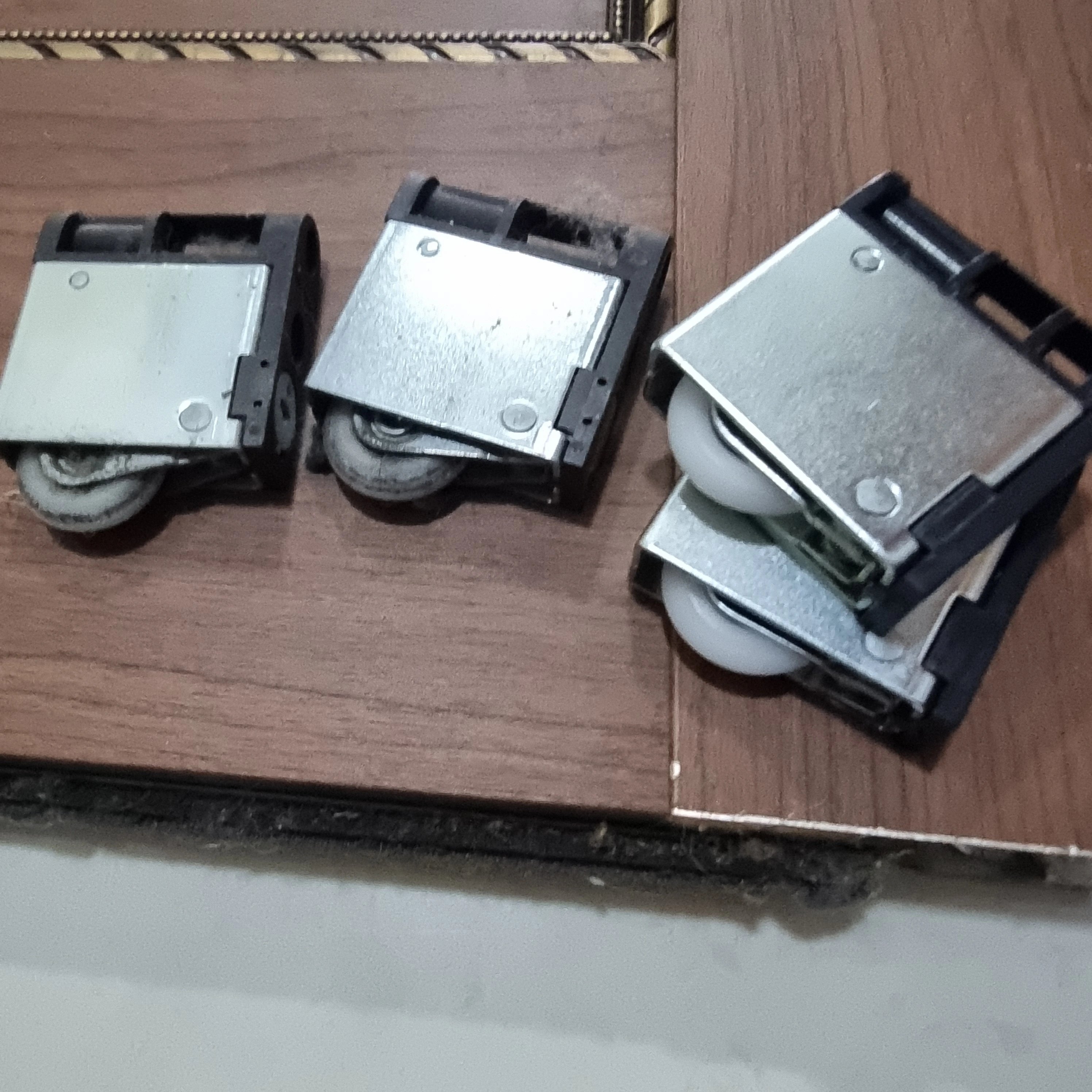 슬라이딩 도어에서 분리한 롤러(바퀴) 부품 세 개를 바닥에 놓고 찍은 사진입니다.