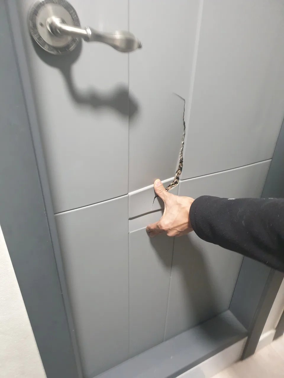 회색 도어 패널 표면에 세로로 갈라진 균열이 생긴 부분을 손으로 짚어 보여주는 사진입니다.