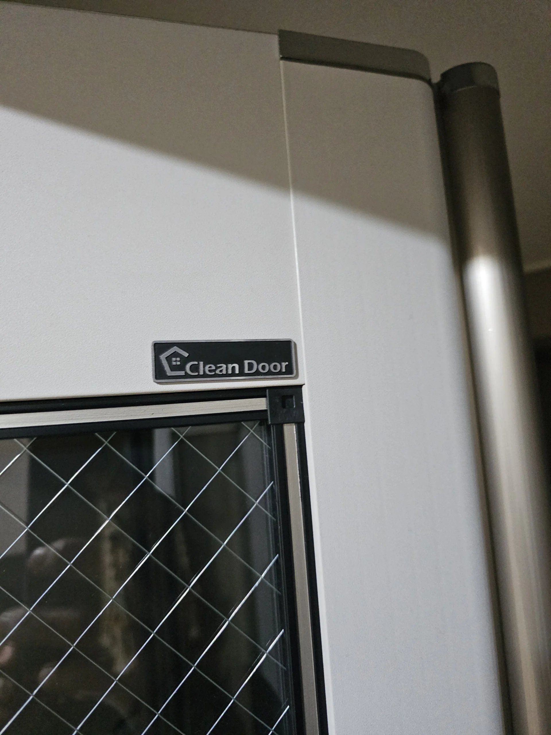 "Clean Door" 라벨이 붙은 흰색 도어 프레임과 그 아래 설치된 방충망형 중문이 보이는 사진입니다.