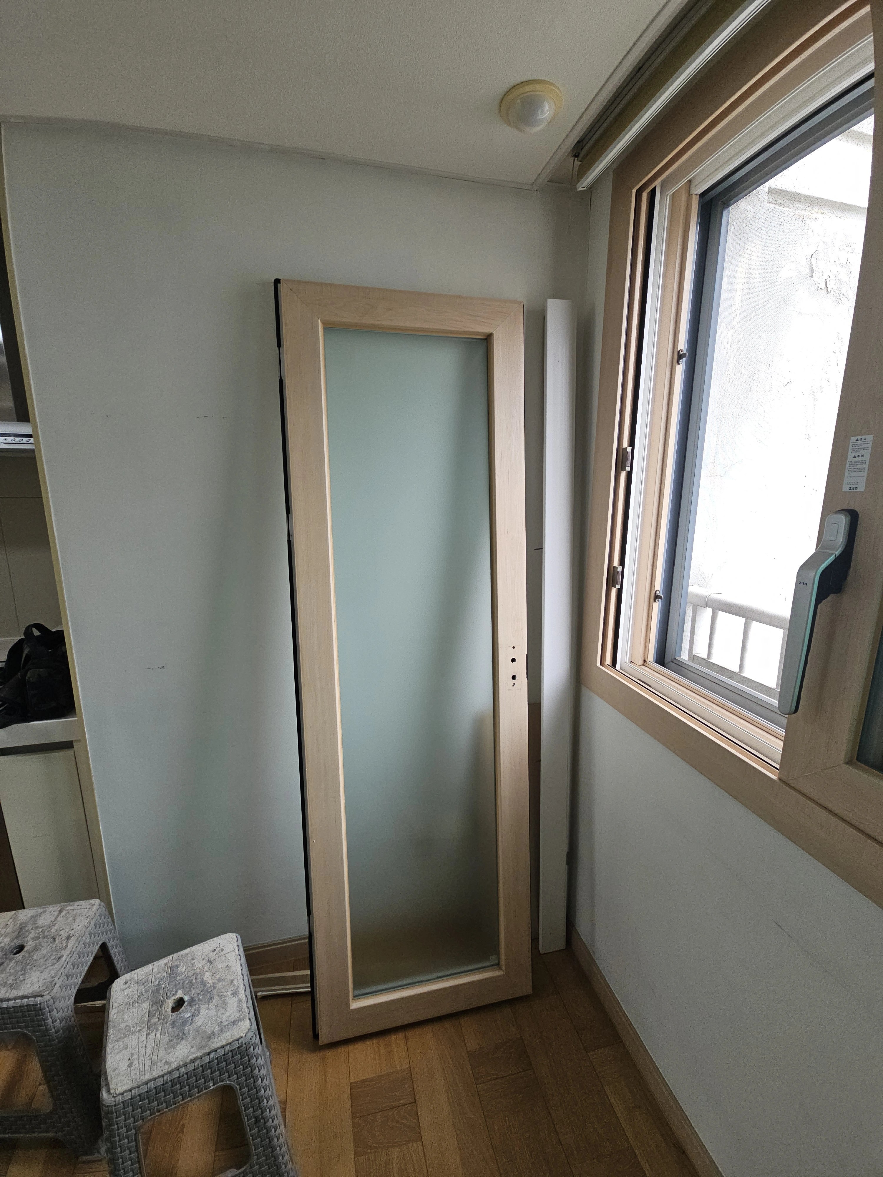 우드 프레임에 불투명 유리가 끼워진 도어 한 짝이 아직 벽에 기대어 세워져 있는 모습입니다.