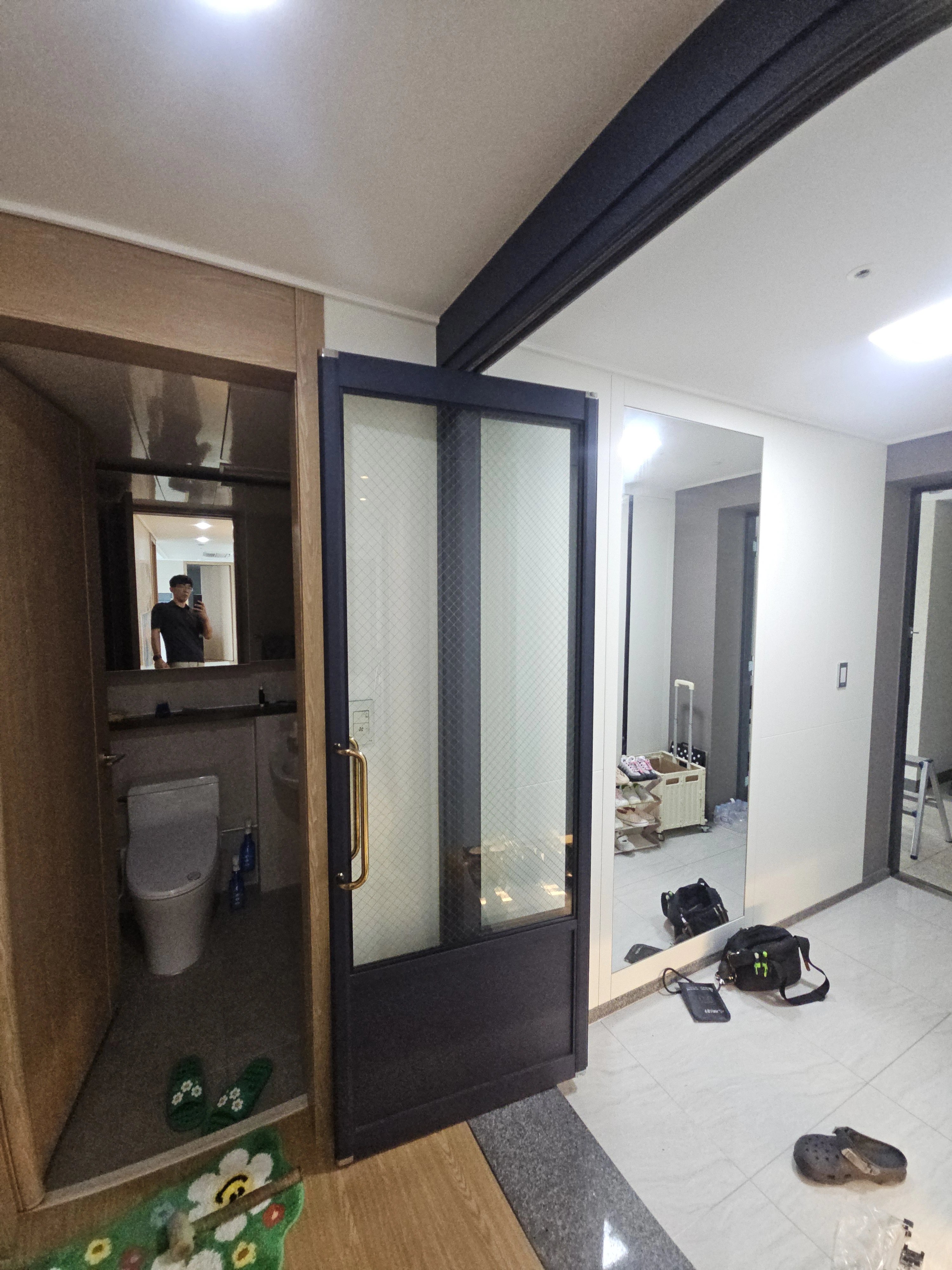 어두운 색 프레임의 유리 여닫이문이 욕실 입구에 설치된 모습입니다.