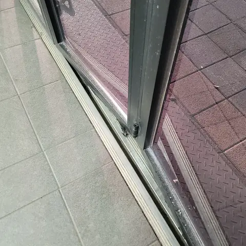 알루미늄 미닫이 샷시 문 밑단 아래 레일 홈에 먼지와 이물이 끼어 있고 롤러 고정 부위가 드러난 모습