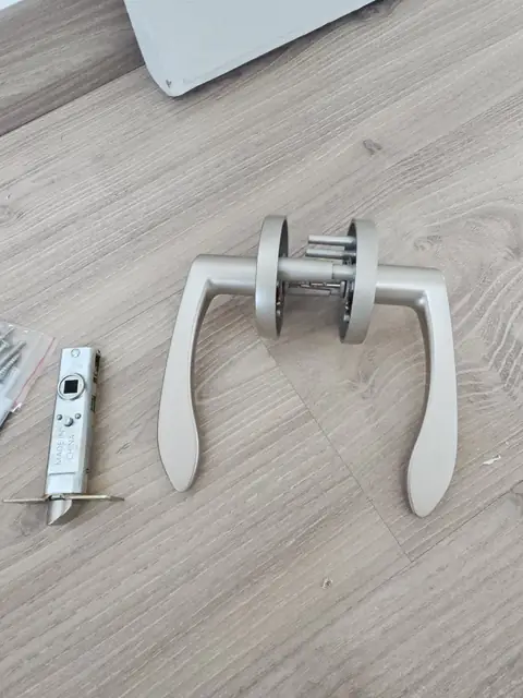 마루 위에 분리한 양쪽 레버와 원형 커버, 모티스 자물쇠 본체와 나사가 놓인 교체 작업 중 사진