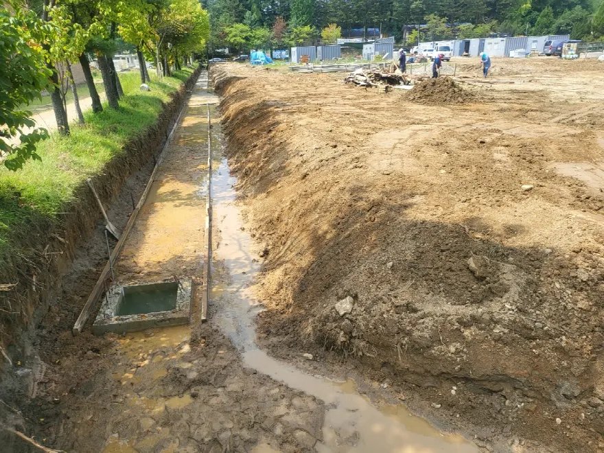부지 경계를 따라 시공된 콘크리트 측구 옆으로 배수 관로용 트렌치를 파 내려간 모습입니다.