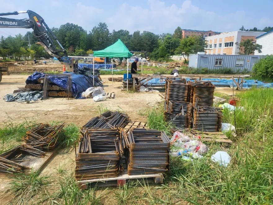 넓은 공사현장에 굴착기와 각종 자재가 놓여 있음.