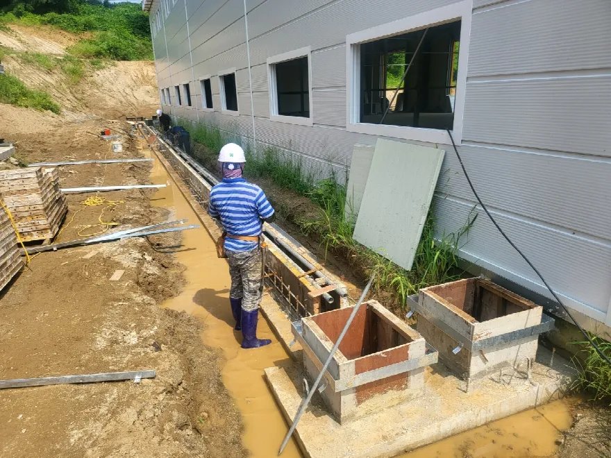 작업자가 안전모와 장화를 착용하고 트렌치 안에서 배수로 라인을 확인하고 있는 장면입니다.