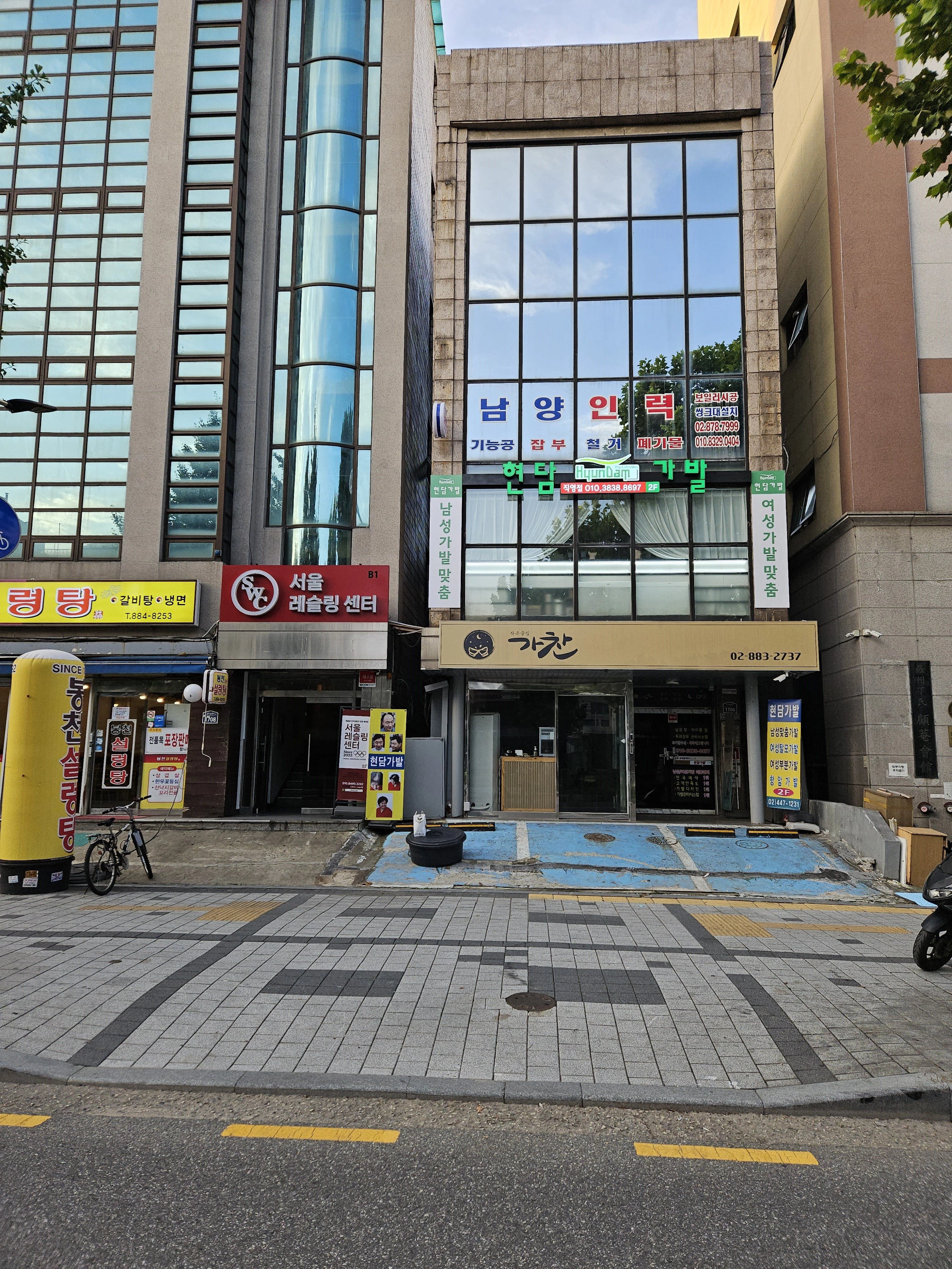 상가 건물 앞 보도블록 바닥에 파란색 테이프로 사각형 구획이 표시되어 있습니다.