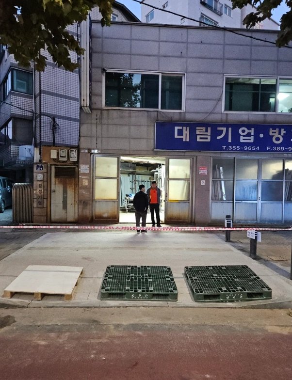새벽 또는 저녁 무렵 상가 건물 입구 앞에서 촬영된 사진으로, 두 사람이 출입구 앞에 서서 이야기를 나누는 모습이 보입니다.