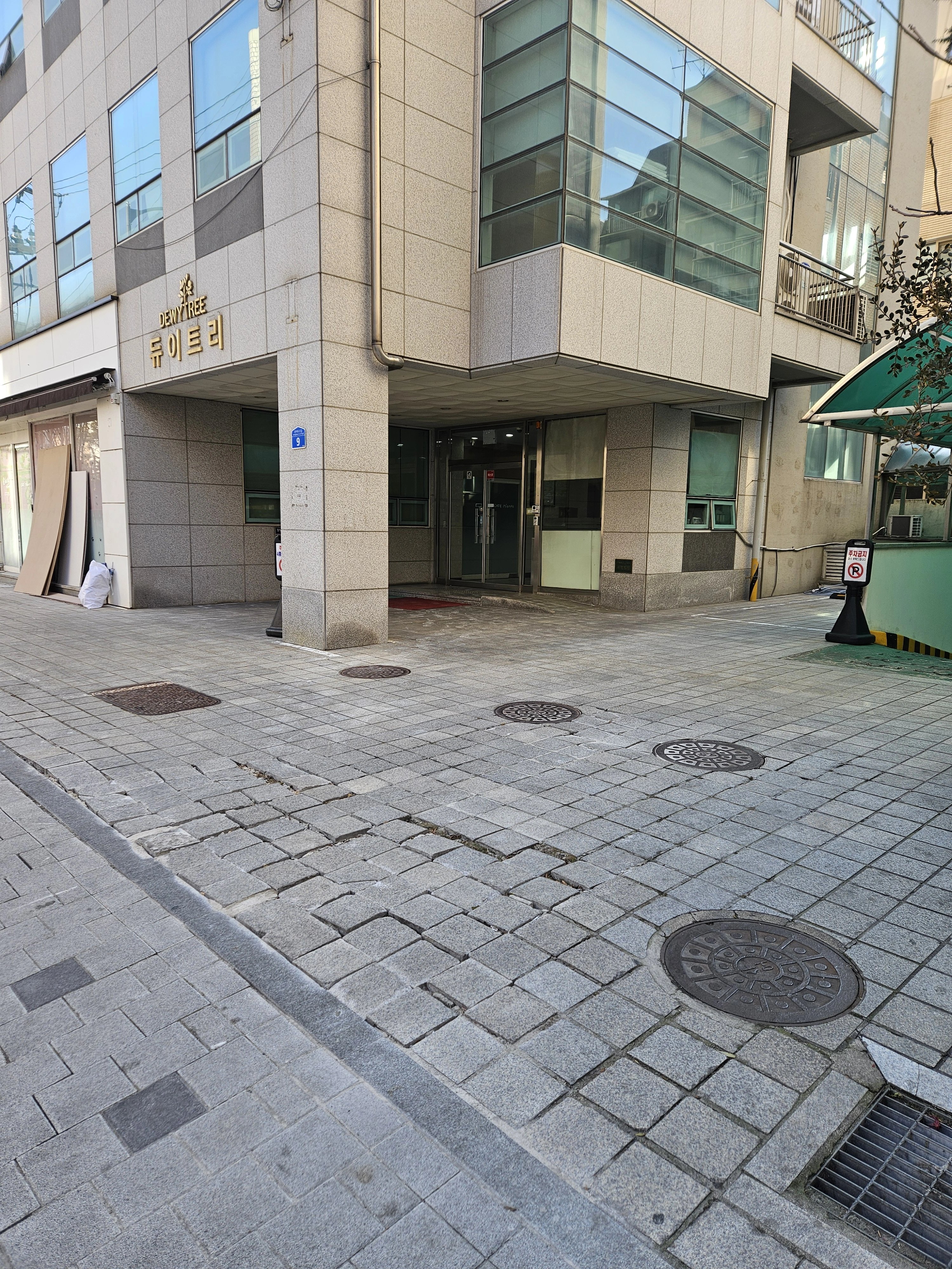 상가 건물 현관 앞으로 차량과 사람이 함께 드나드는 통로를 블록으로 포장한 모습입니다.