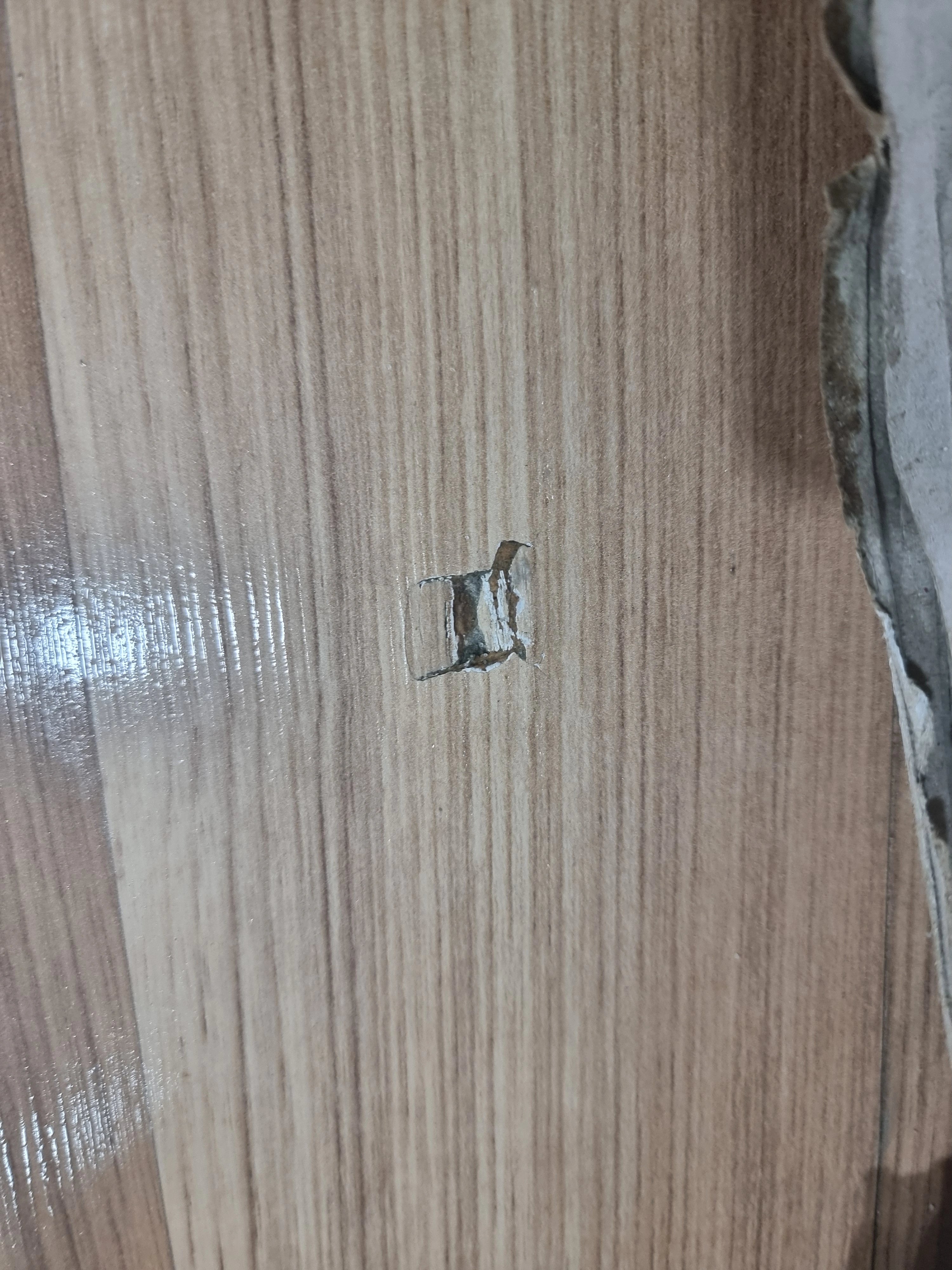 나무 무늬 바닥재 표면에 작은 사각형 모양의 구멍이 뚫려 있고 가장자리가 들뜬 상태가 보입니다.