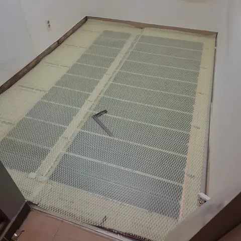 실내 바닥 전체에 단열재로 보이는 판을 깔고 와이어메쉬를 촘촘히 덮은 뒤 벽 테두리를 따라 마감선을 잡아 둔 기초 작업
