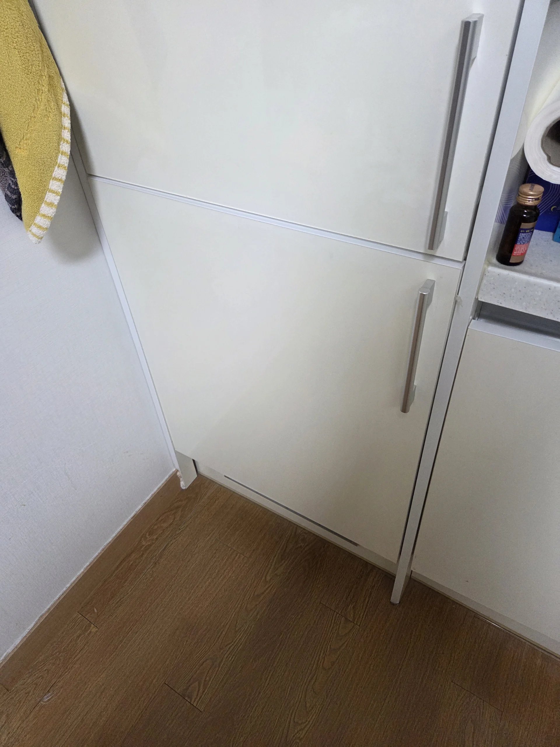 위아래 두 칸으로 된 흰색 빌트인 냉장고 문 가운데 아래 문짝이 비스듬히 내려앉은 모습입니다.