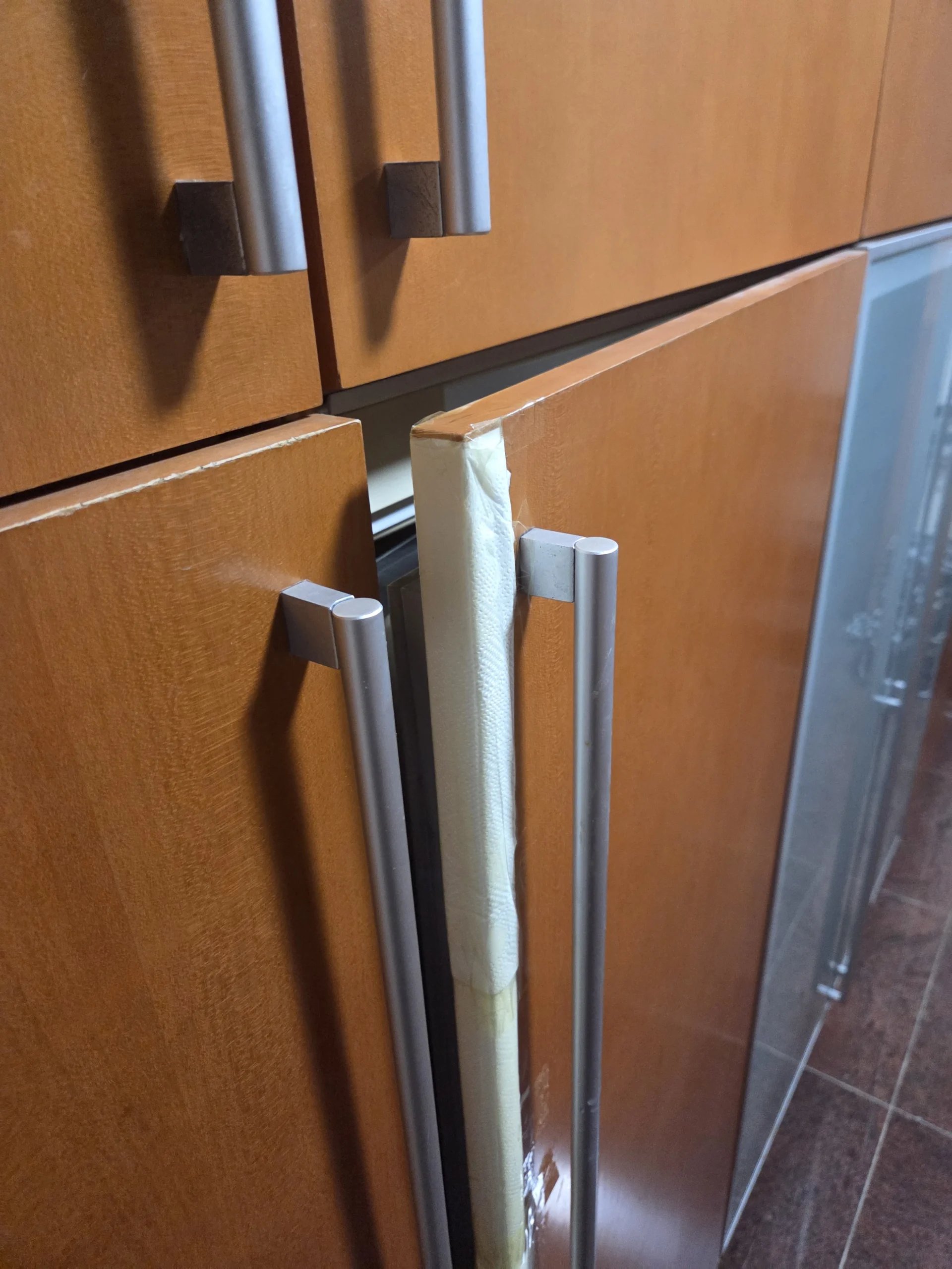 나무결 냉장고장의 키 큰 양문 중 오른쪽 문이 처져 닫히지 않고 비스듬히 열려 있는 모습입니다.