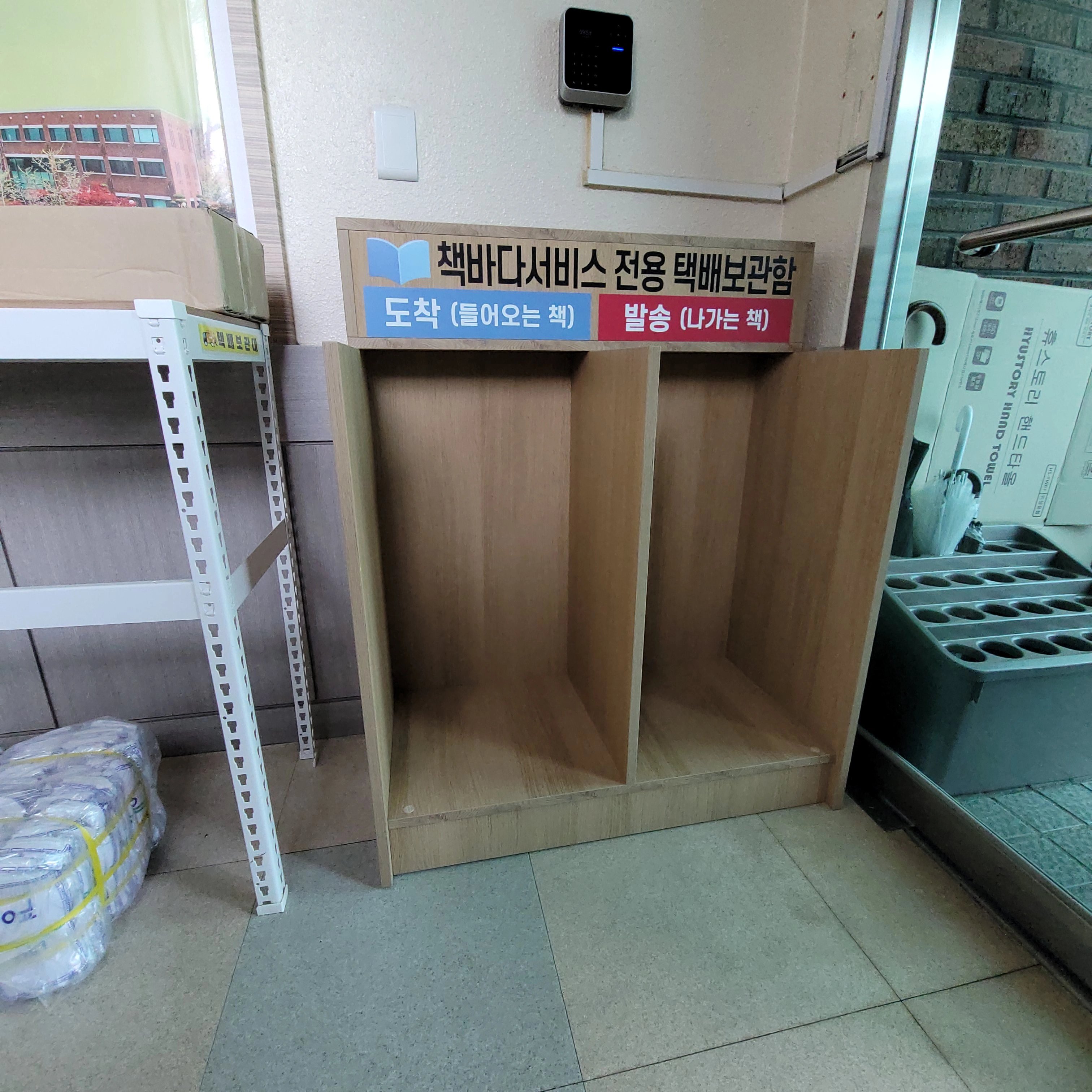 목재로 짠 칸막이형 수납장이 바닥에 놓여 있고 상단에 용도를 안내하는 표지판이 부착되어 있다.