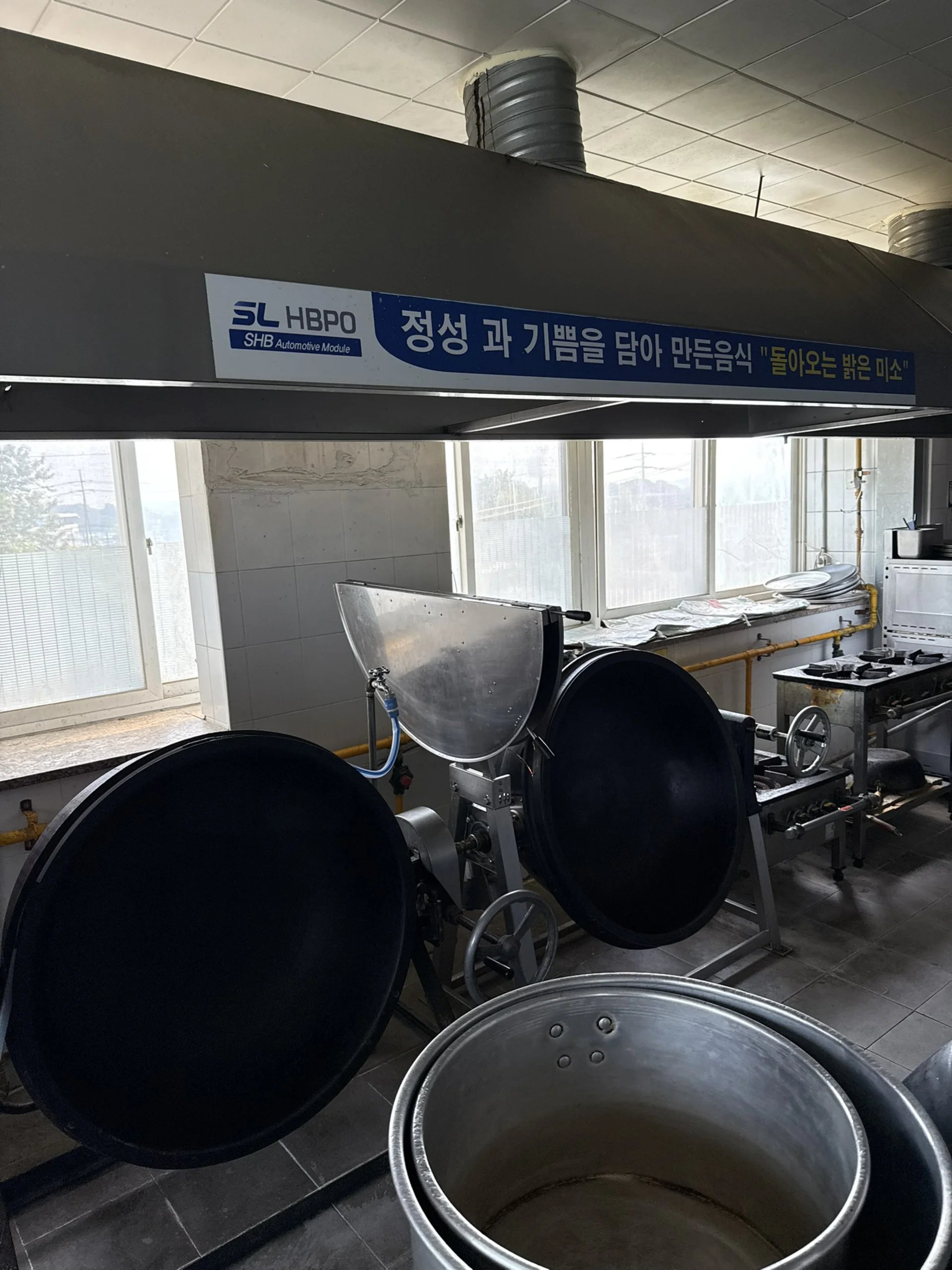 창문이 많은 공장형 조리 공간 천장에 원형 플렉시블 덕트를 연결해 환기 라인을 설치한 모습입니다.