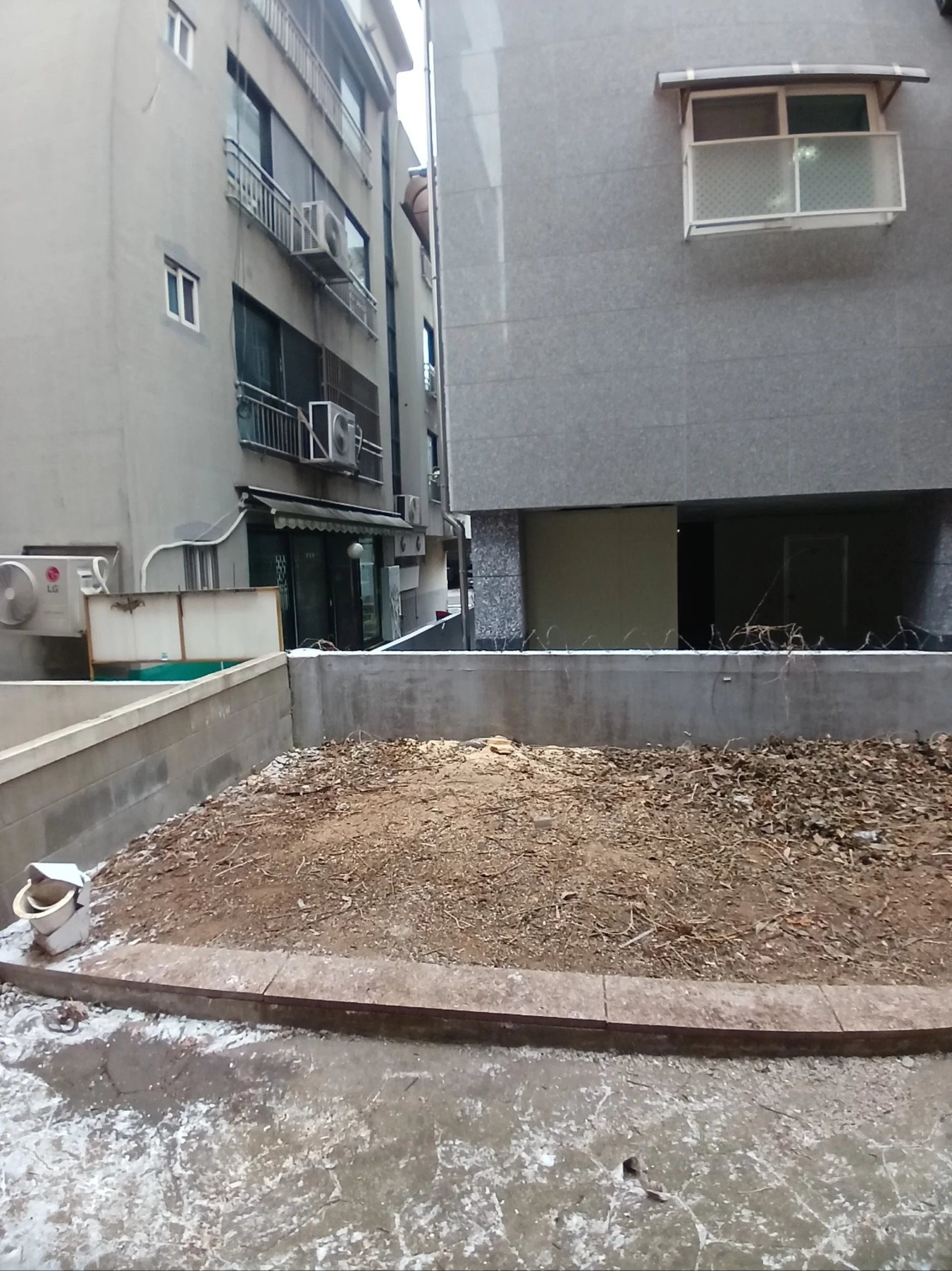 건물 사이 공터의 식재나 잡목을 정리하고 흙바닥만 남은 상태를 보여주는 사진이다.