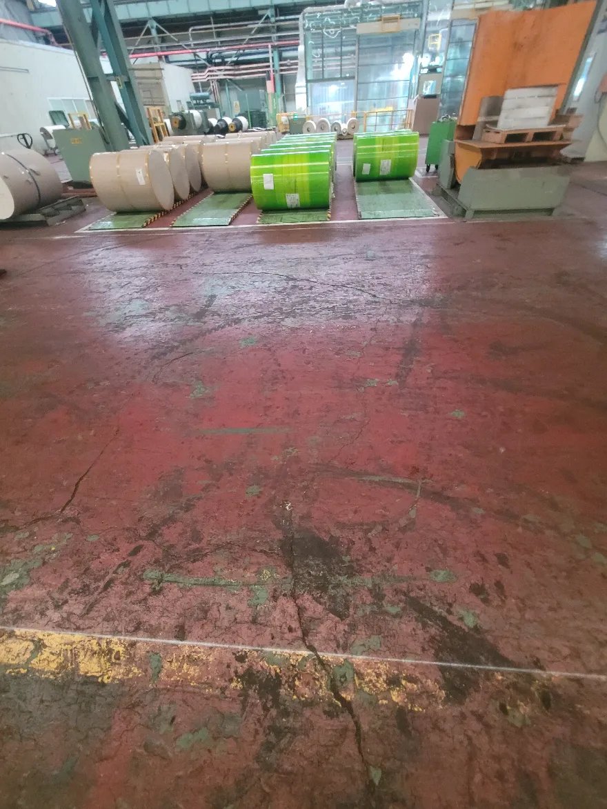 코일 자재가 늘어선 공장 안에서 붉은 바닥면의 마모 상태를 살핀 장면입니다.