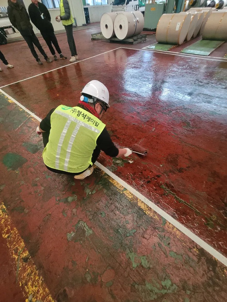 안전조끼를 입은 작업자가 앉아서 소형 롤러로 경계 부위 재료를 밀어 바르고 있습니다.