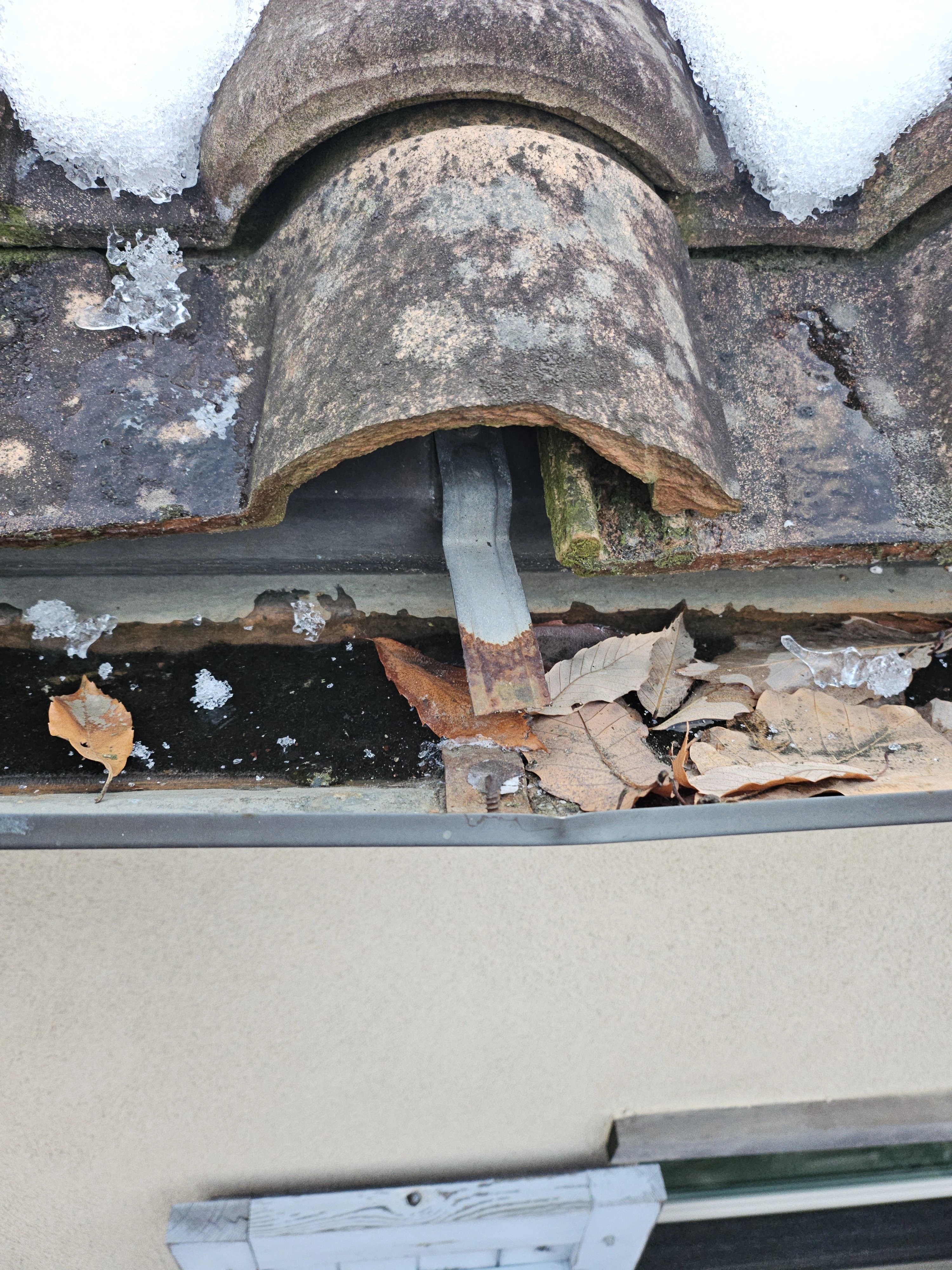 기와지붕 처마 끝 홈통 부분을 근접 촬영한 사진으로, 낙엽과 잔가지가 수로 안에 가득 쌓여 있는 모습이 보입니다.