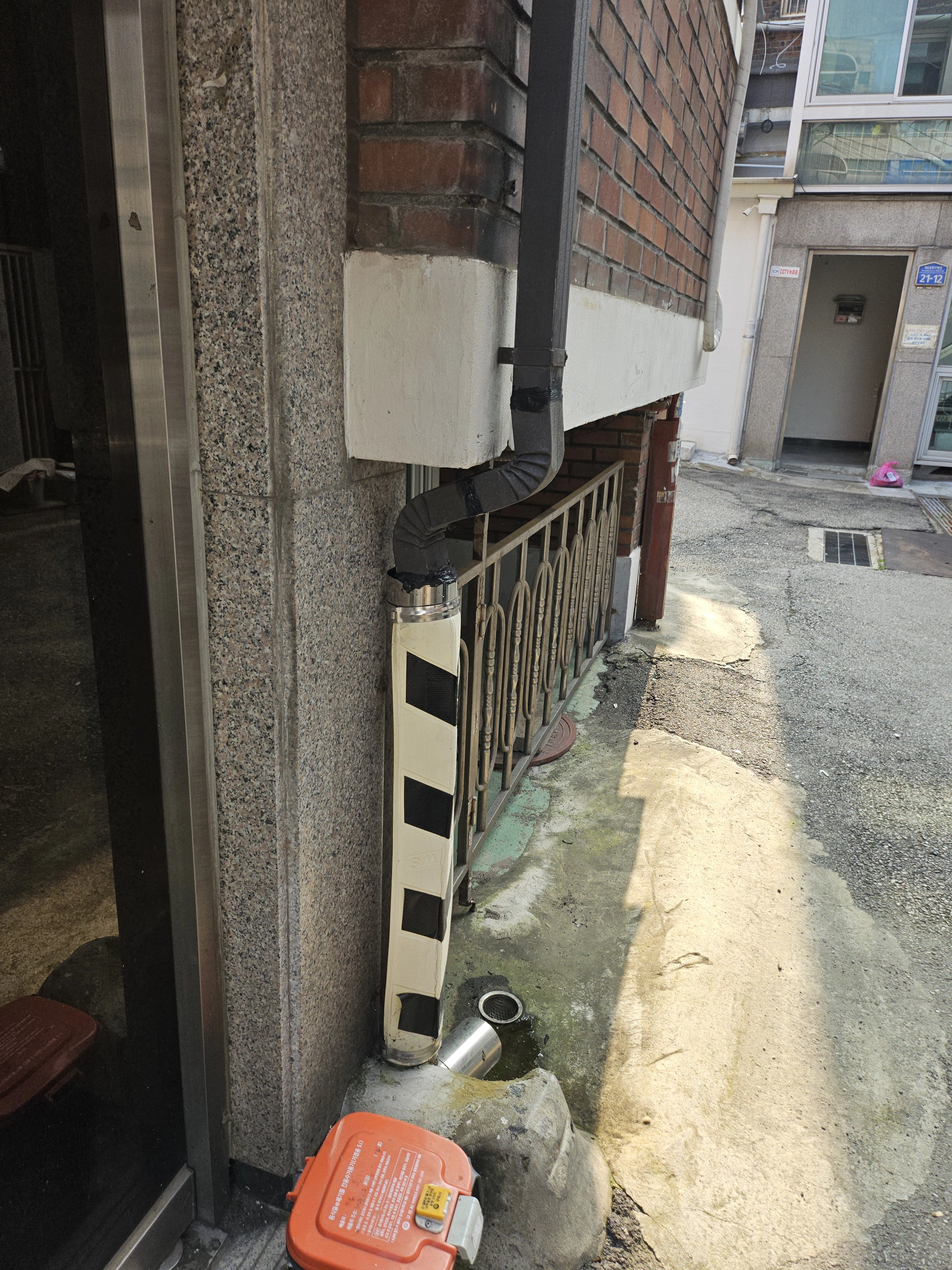 건물 처마 하부 배수 박스에서 내려오는 우수관이 엘보로 방향을 꺾어 벽을 따라 수직으로 연결되어 있습니다.