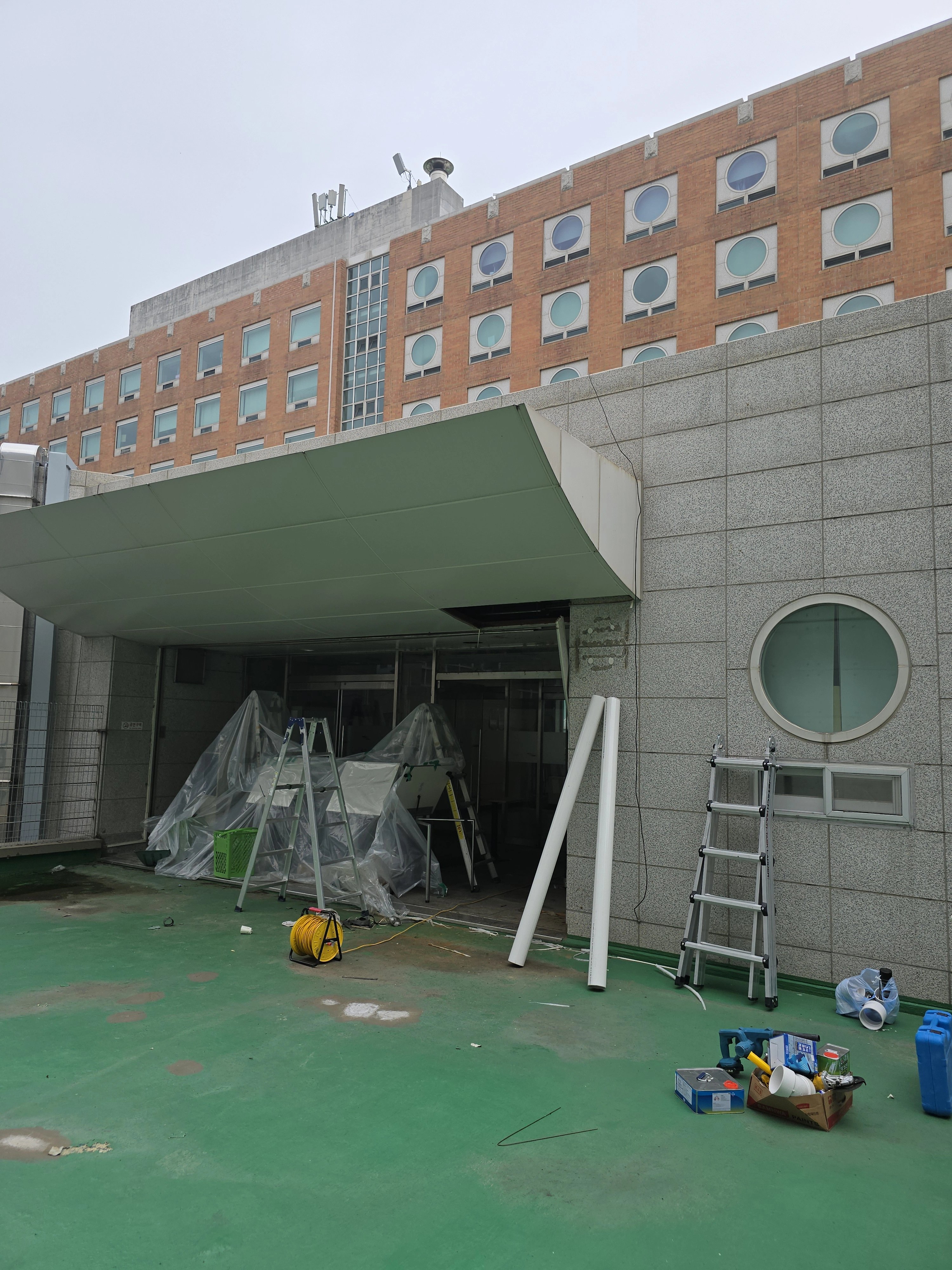 건물 출입구 캐노피 아래쪽 공간에서 작업을 준비 중인 모습입니다.