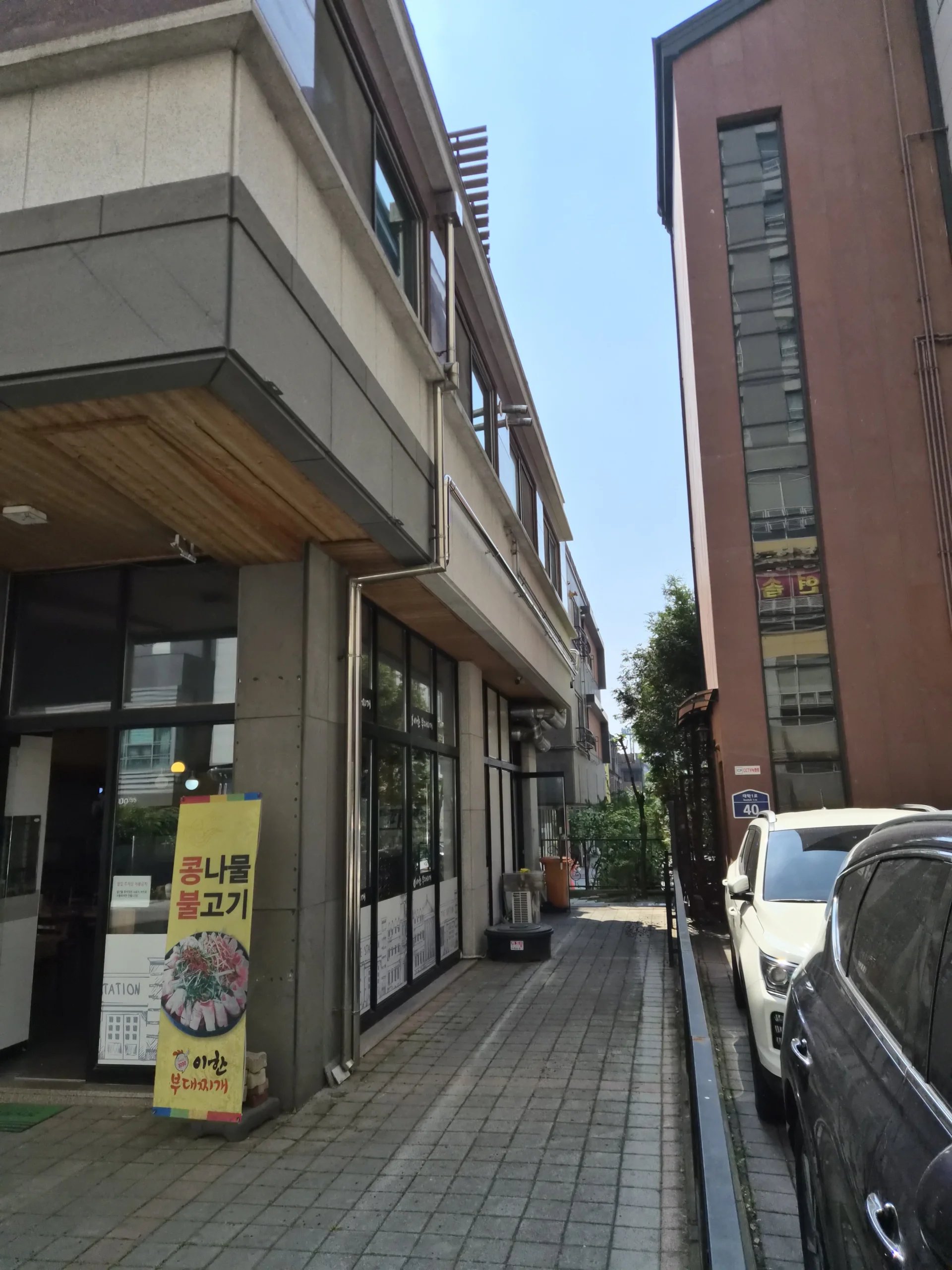 상가 건물 1층 처마 아래를 따라 회색 우수관이 수평으로 길게 연결된 뒤 모서리에서 수직으로 꺾여 내려가는 모습입니다.