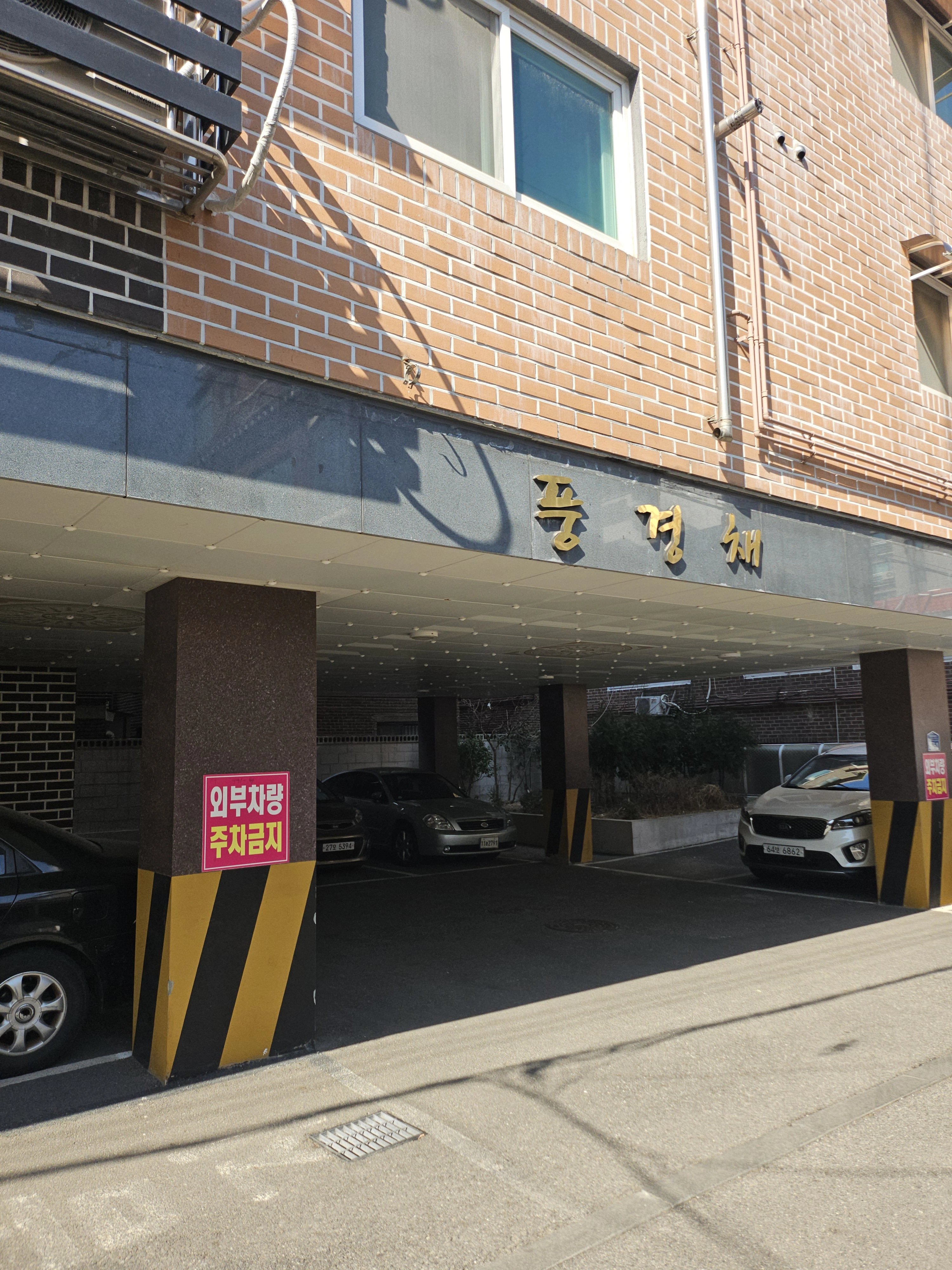 벽돌 마감 건물의 필로티 주차장 진입부를 도로 쪽에서 본 사진입니다.
