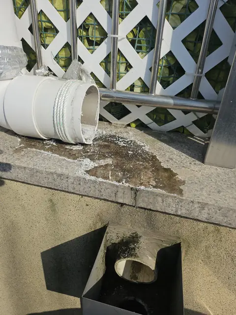 외벽 하단 석재 걸레받이 위에 흰 PVC 곡관이 아직 이어지지 않은 채 놓여 있고 아래로 매립된 사각 집수구 박스와 원형 배출구가 드러난 모습