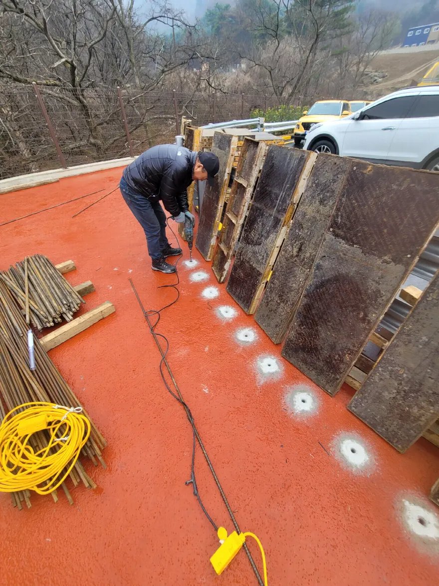 보도 바닥을 따라 앵커 구멍이 일정한 간격으로 줄지어 뚫려 있고 주변에 흰 천공 가루가 국화처럼 퍼져 있습니다.