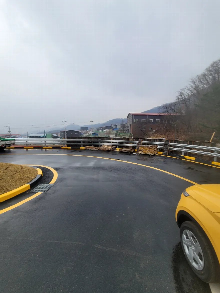 새로 포장하고 도색한 곡선 도로 안쪽에서 작업 구간 쪽을 바라본 사진입니다.