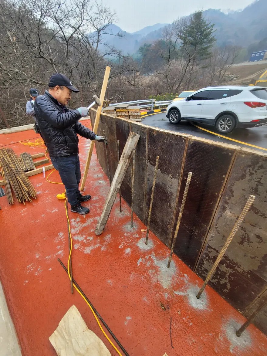 작업자가 긴 각목을 세워 거푸집 안쪽에 버팀재로 대고 있는 장면입니다.