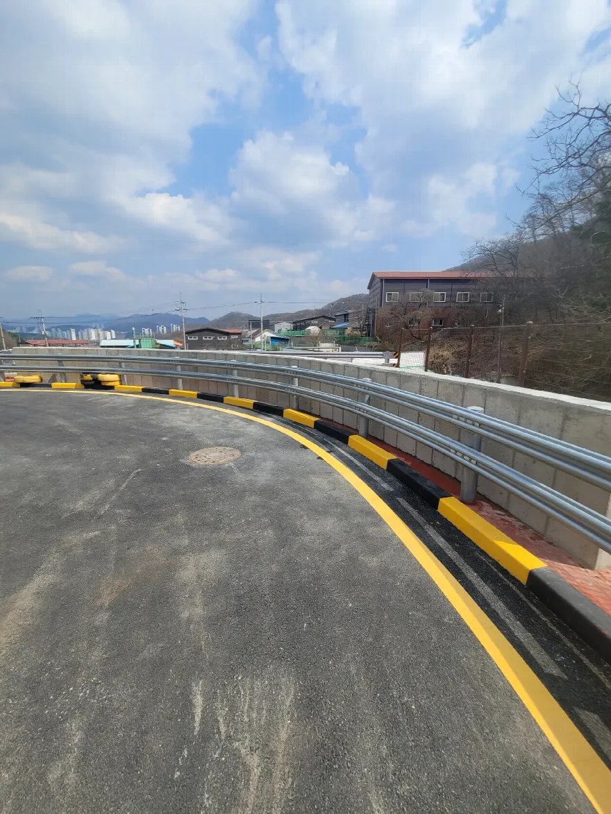 옹벽과 도로 포장, 안전시설이 모두 끝난 구간을 낮은 눈높이에서 본 완료 사진입니다.