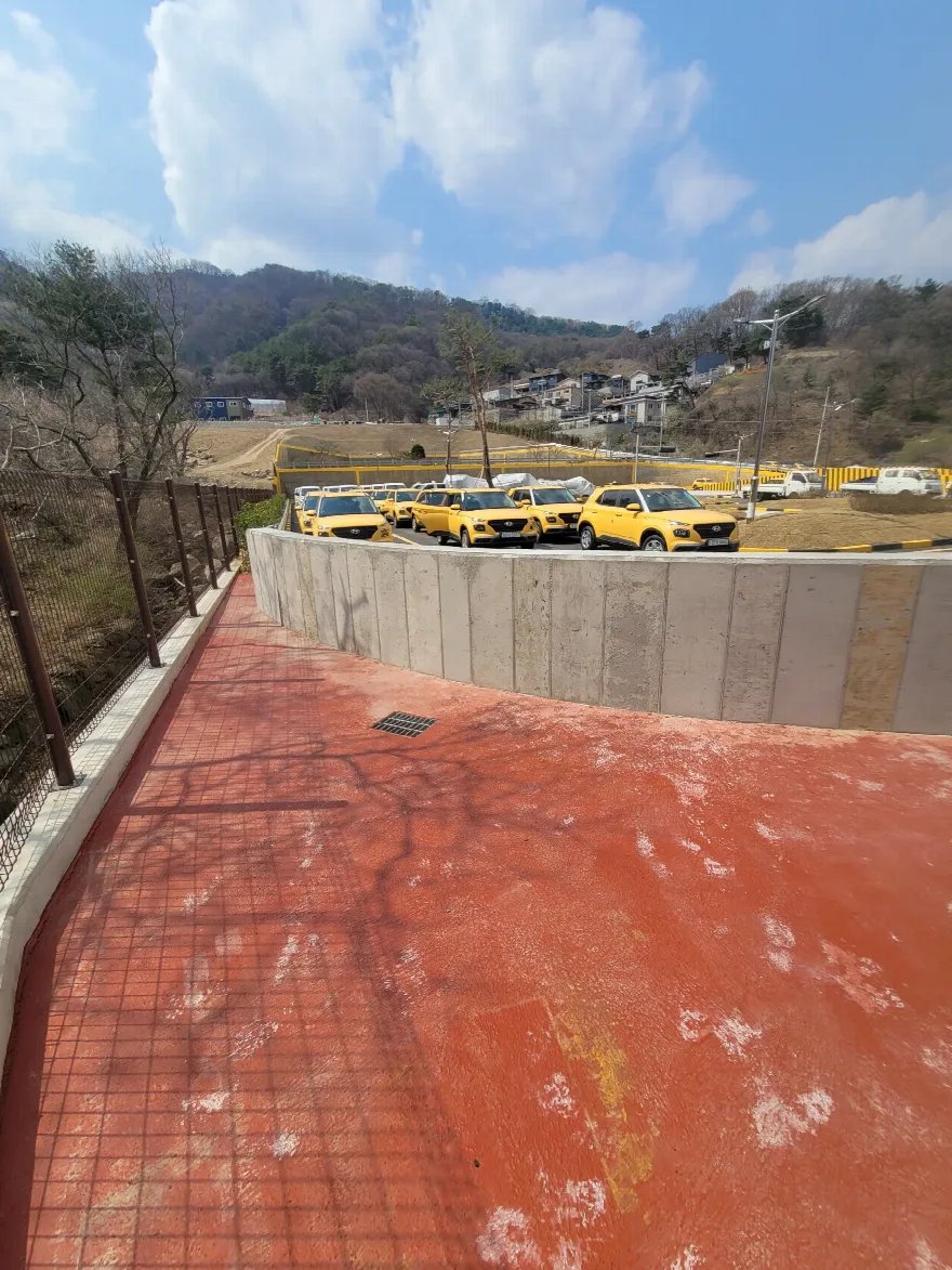 탈형이 끝난 콘크리트 옹벽과 그 안쪽 붉은 포장 마당을 함께 담은 사진입니다.