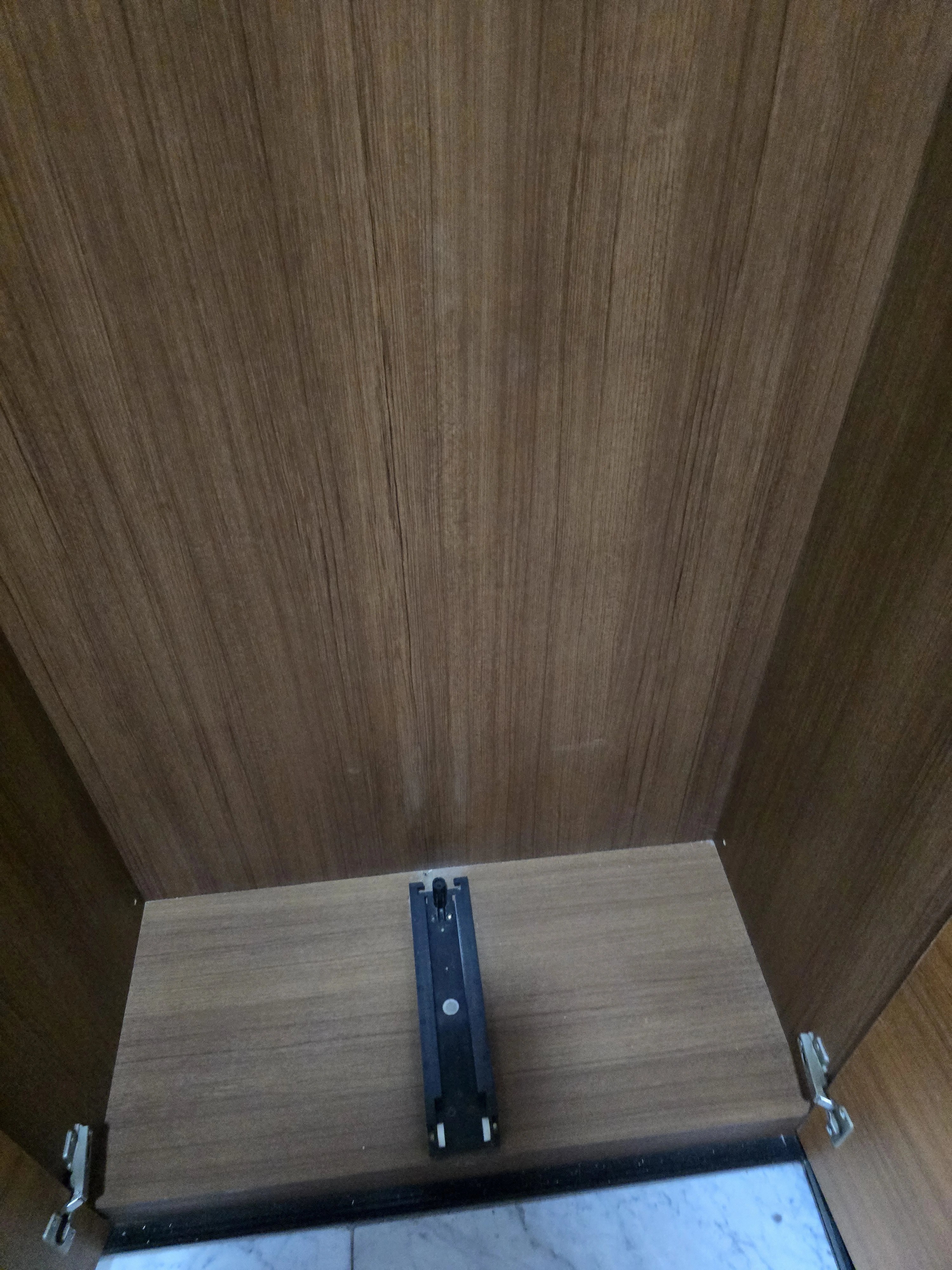 신발장 하단부를 위에서 내려다보듯 가까이 찍은 사진으로, 바닥면에 설치된 검은색 경첩·완충 장치가 중앙에 보입니다.