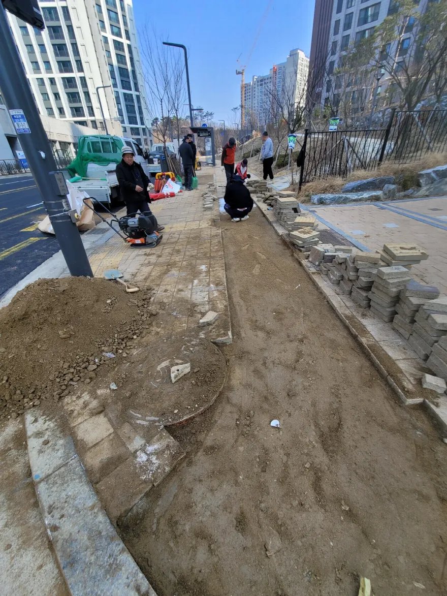 블록을 걷어낸 보도에 기층 흙을 정리하고 다짐 장비로 다지는 시공 중 장면입니다.