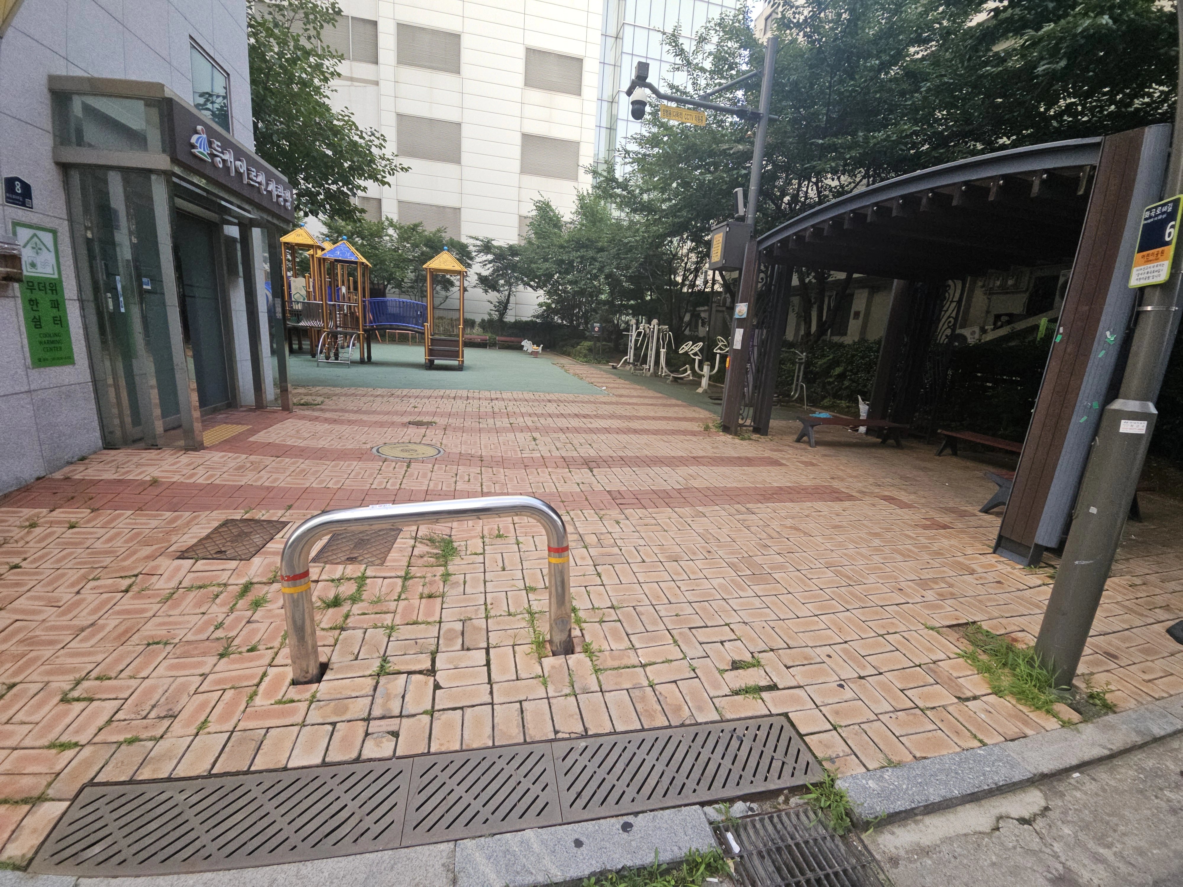 보도블럭이 깔린 광장형 보행로를 촬영한 사진으로, 블록 사이 줄눈을 따라 잡초가 올라와 있는 모습이 눈에 띕니다.