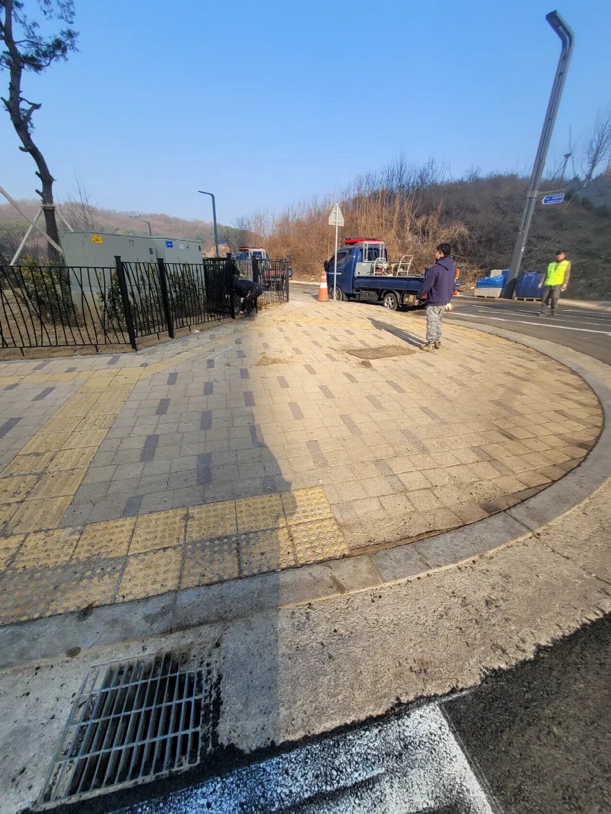 교차로 모퉁이 인도 시공이 마무리된 모습으로, 황색 블록과 진한 띠 패턴, 노란 점자블록이 곡선 경계석 안쪽에 빈틈없이 채워져 있습니다.