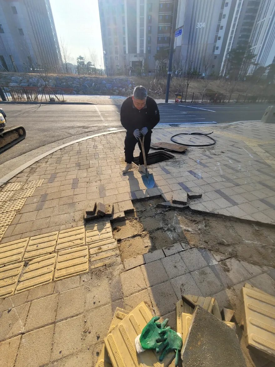 곡선 보도 모서리의 블록을 삽으로 하나씩 들어내는 철거 작업 장면입니다.
