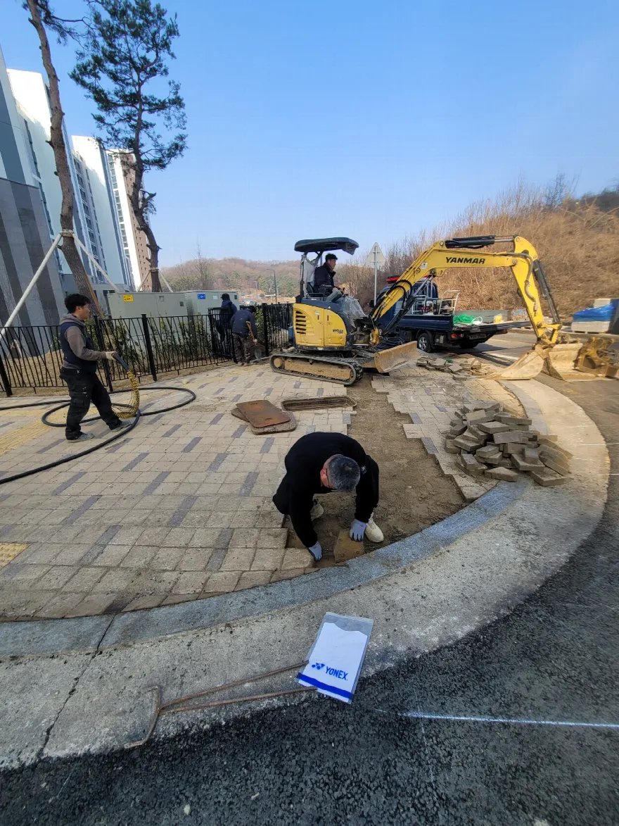 곡선 보도 모서리 구간을 소형 굴삭기와 인력으로 함께 걷어내는 철거 단계입니다.
