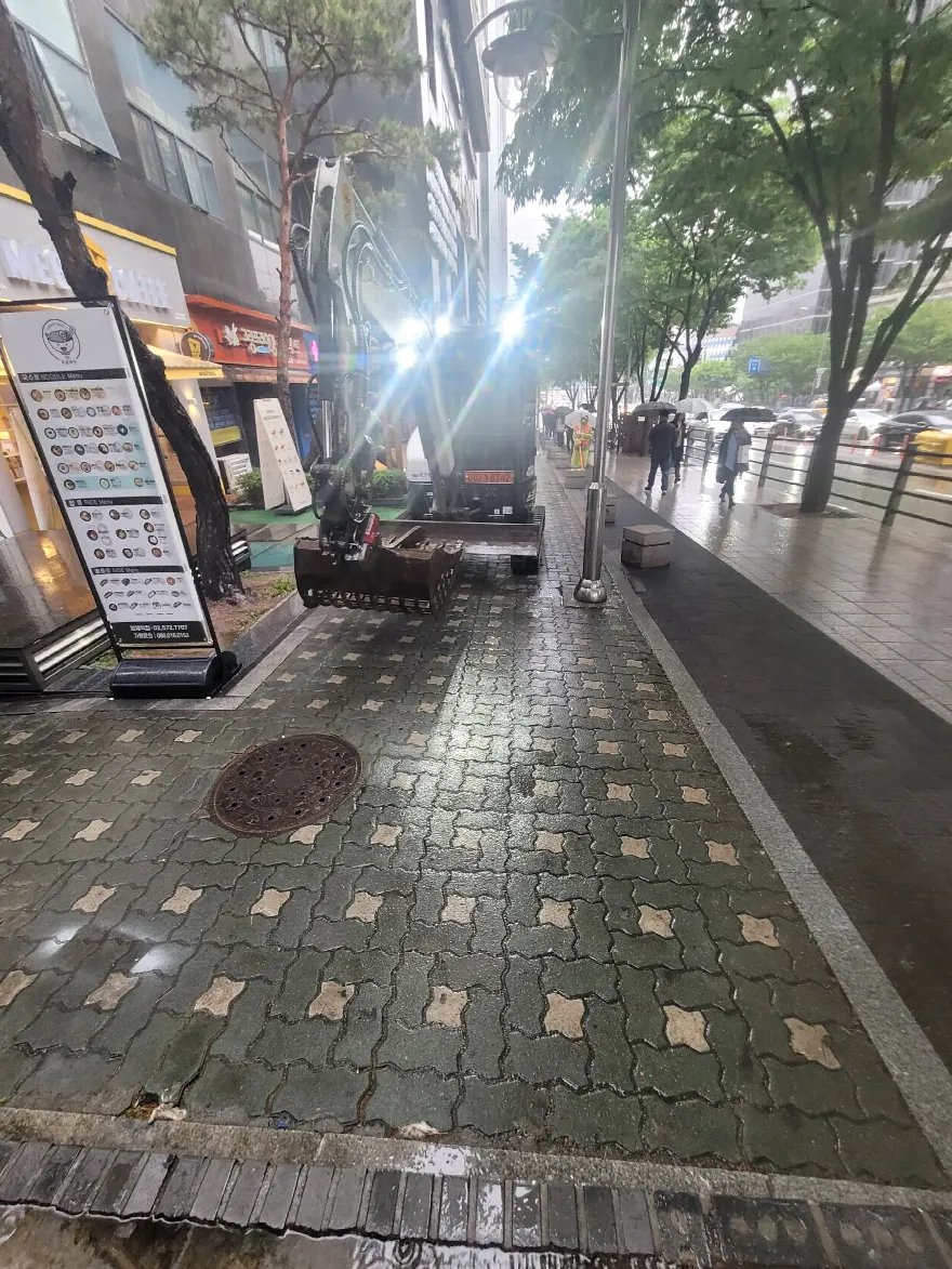 우천 중 상가 앞 보도에 소형 굴삭기가 들어와 있는 모습입니다.