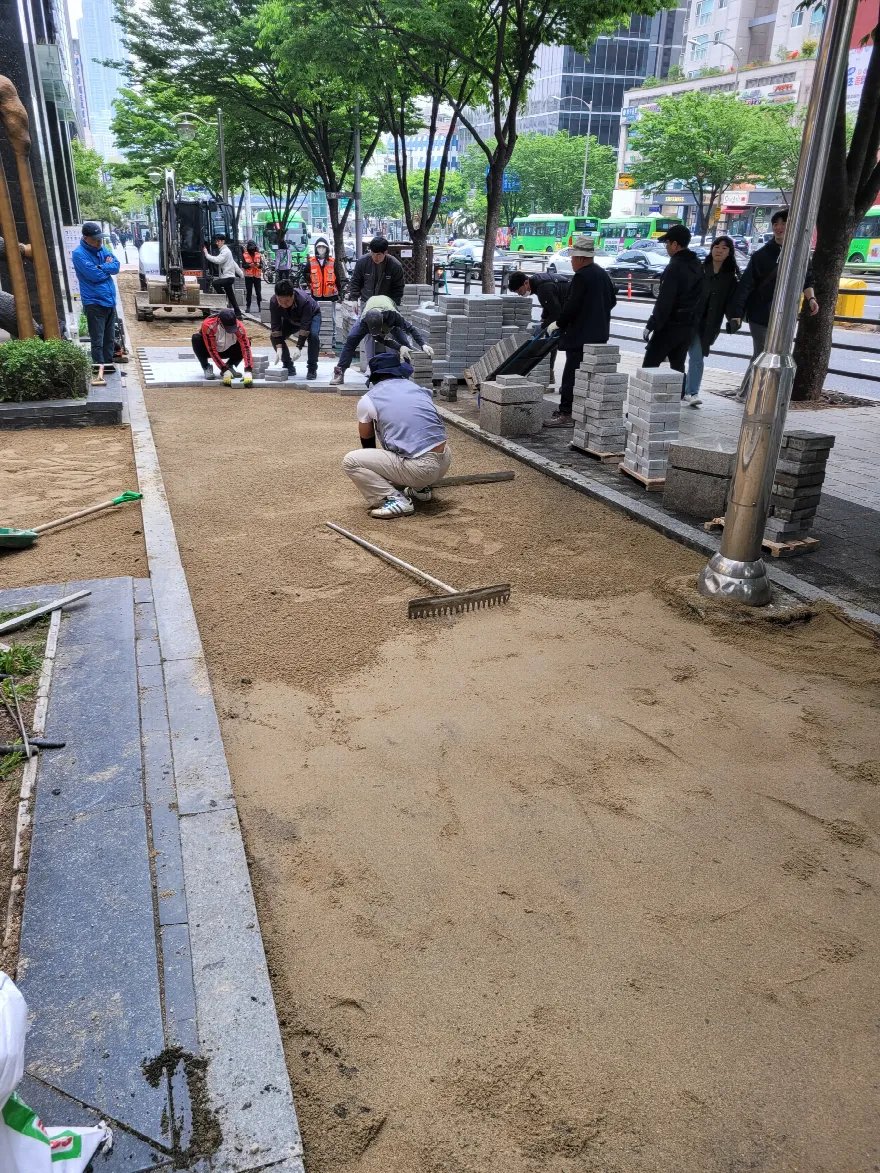 가로수가 늘어선 대로변 인도에서 모래 포설과 평탄 작업이 한창입니다.
