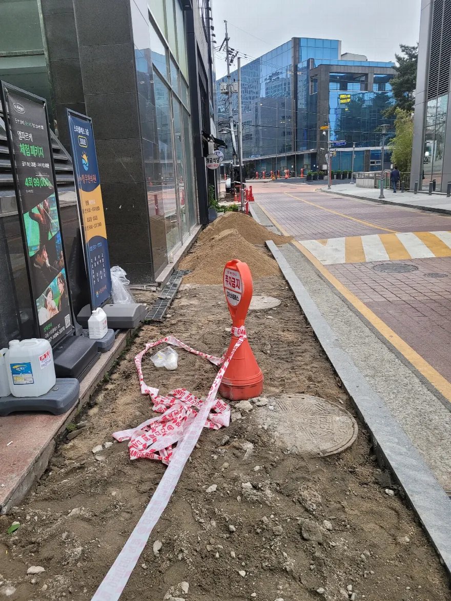 건물 앞 인도의 기존 블록을 걷어낸 상태로, 흙바닥이 드러나 있고 굵은 돌과 잔재가 섞여 있습니다.