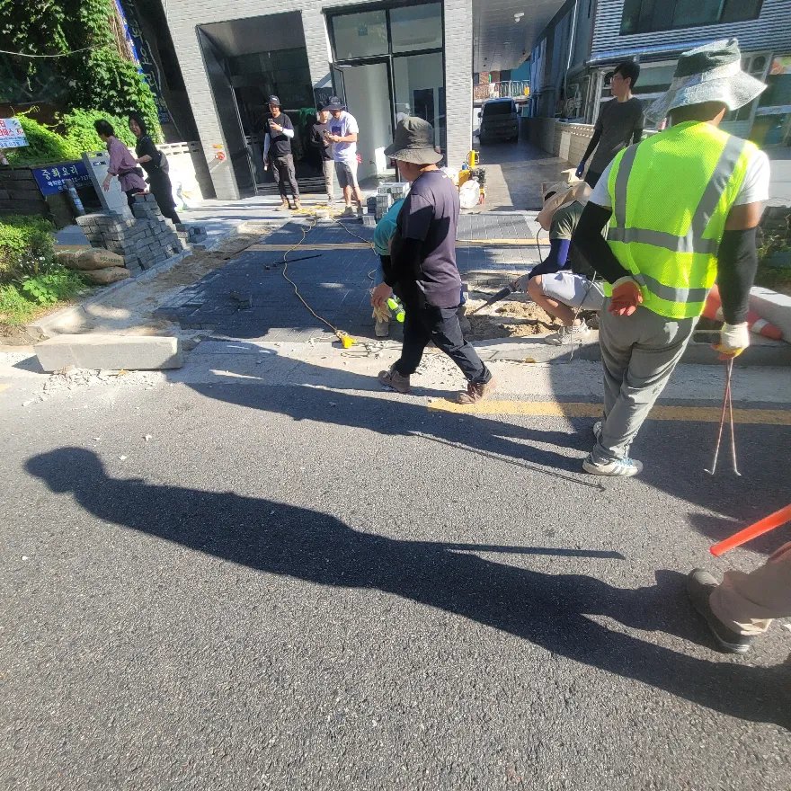 건물 입구 앞 보도의 도로 접속부에서 작업자 여러 명이 작업 중인 장면입니다.