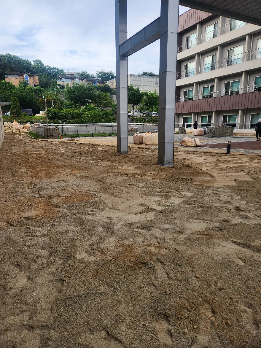 건물 앞 넓은 외부 공간에 보도블럭을 깔기 위해 모래 기층을 포설해 둔 준비 단계입니다.