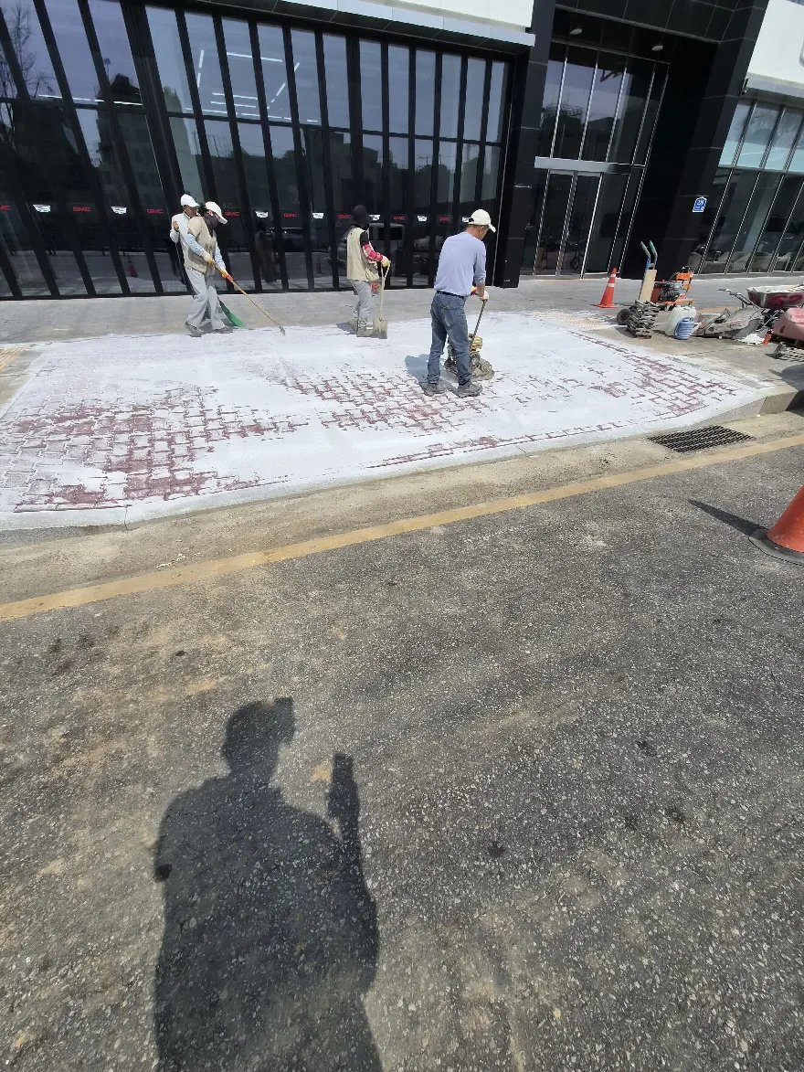 붉은 계열 블럭을 다 깔아 놓은 면 위로 흰 가루를 뿌리고 빗자루로 쓸어 넣는 줄눈 채움 작업이 보입니다.